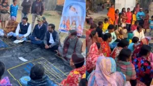 Community meeting outdoors with seated participants.